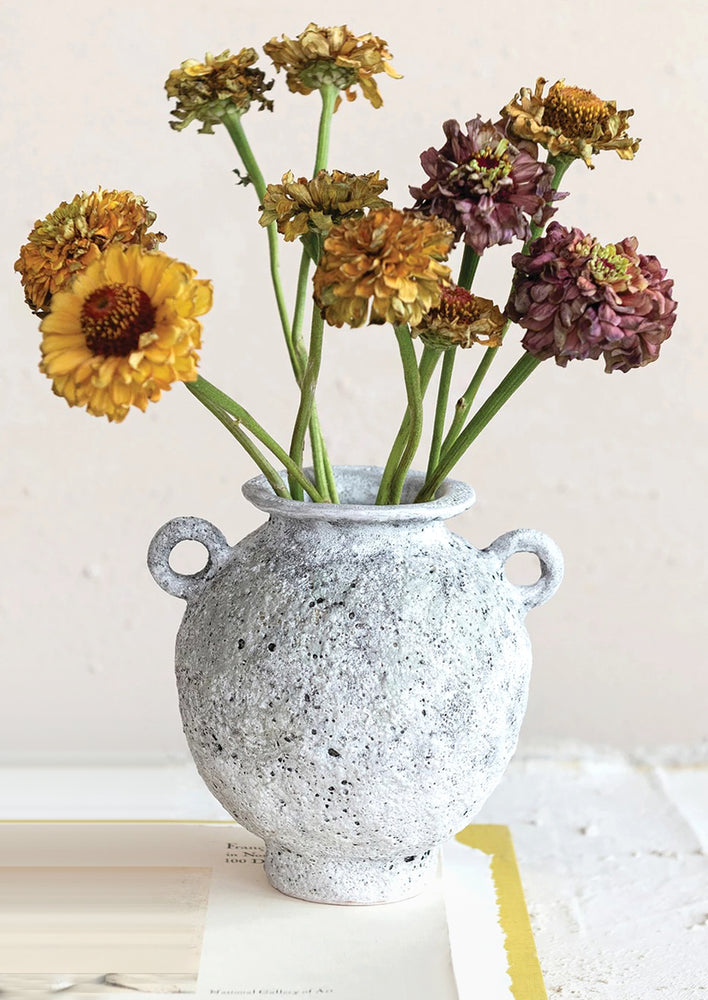 A vase in rough textured gray glaze, small side loop handles, holding dried zinnia flowers.