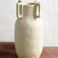 2: A sand color vase in matte ceramic with decorative square handle detail around mouth.