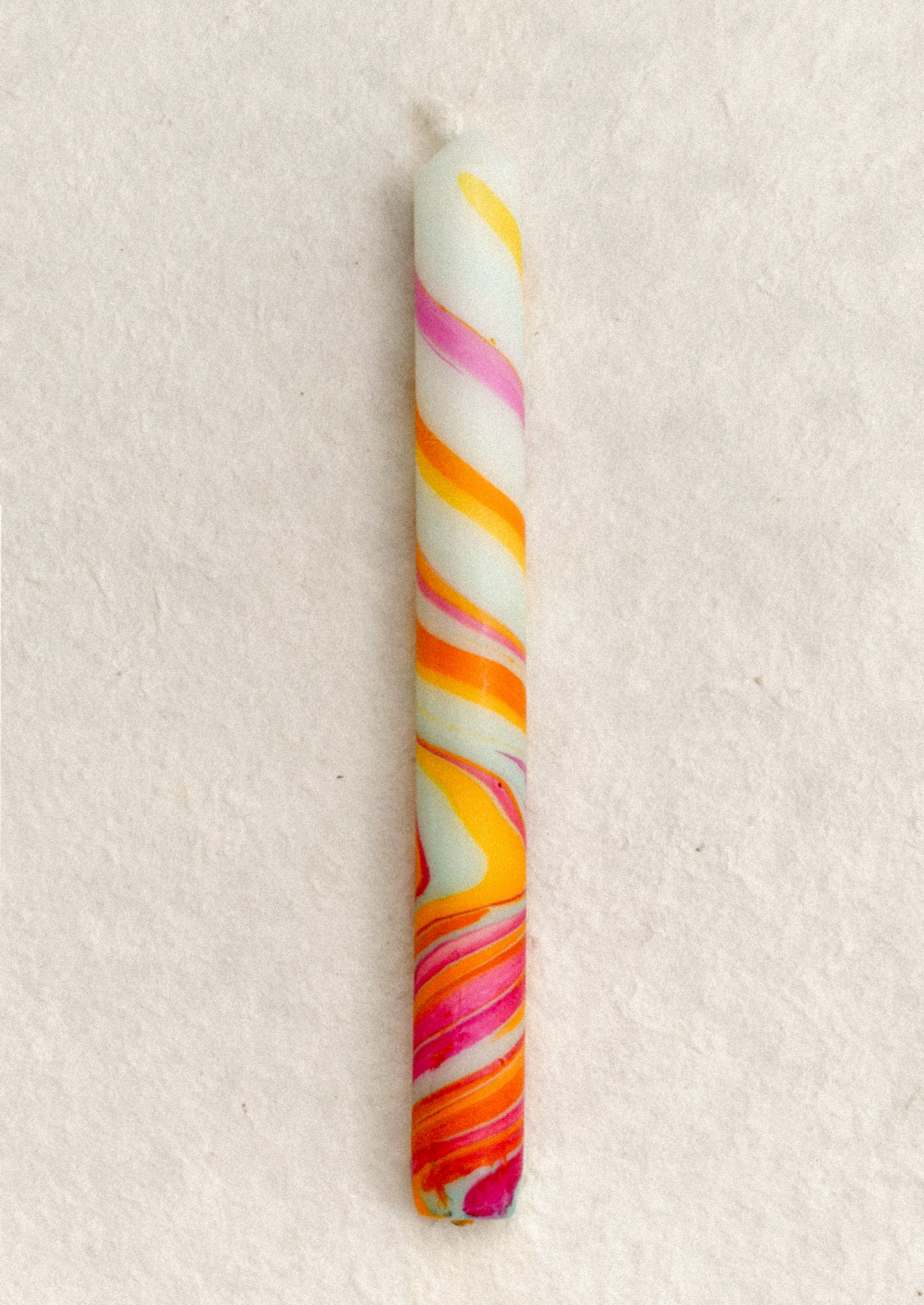 A marbled taper candle in pink, orange, yellow and aqua swirl pattern.