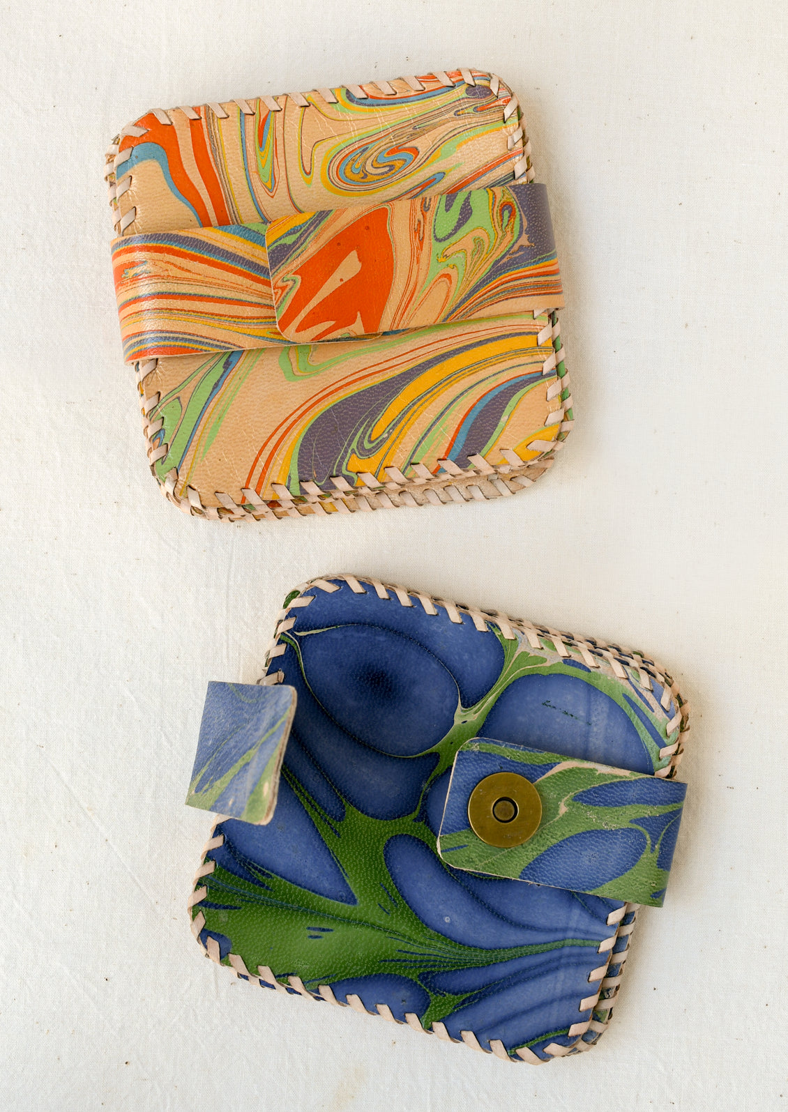 Two colorful marbled square leather coaster sets with whipstitched edges and a matching wraparound strap.