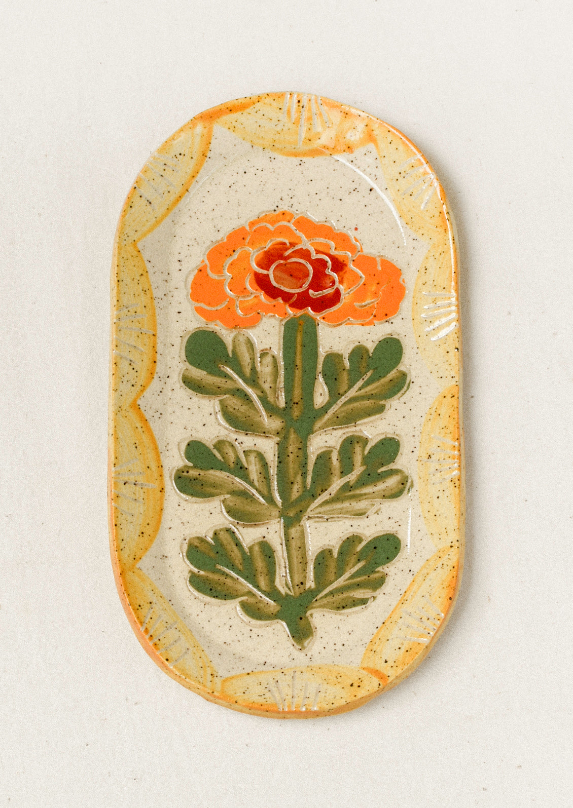 A ceramic oval catchall tray with an etched yellow marigold flower in the center and a yellow painted scallop border.
