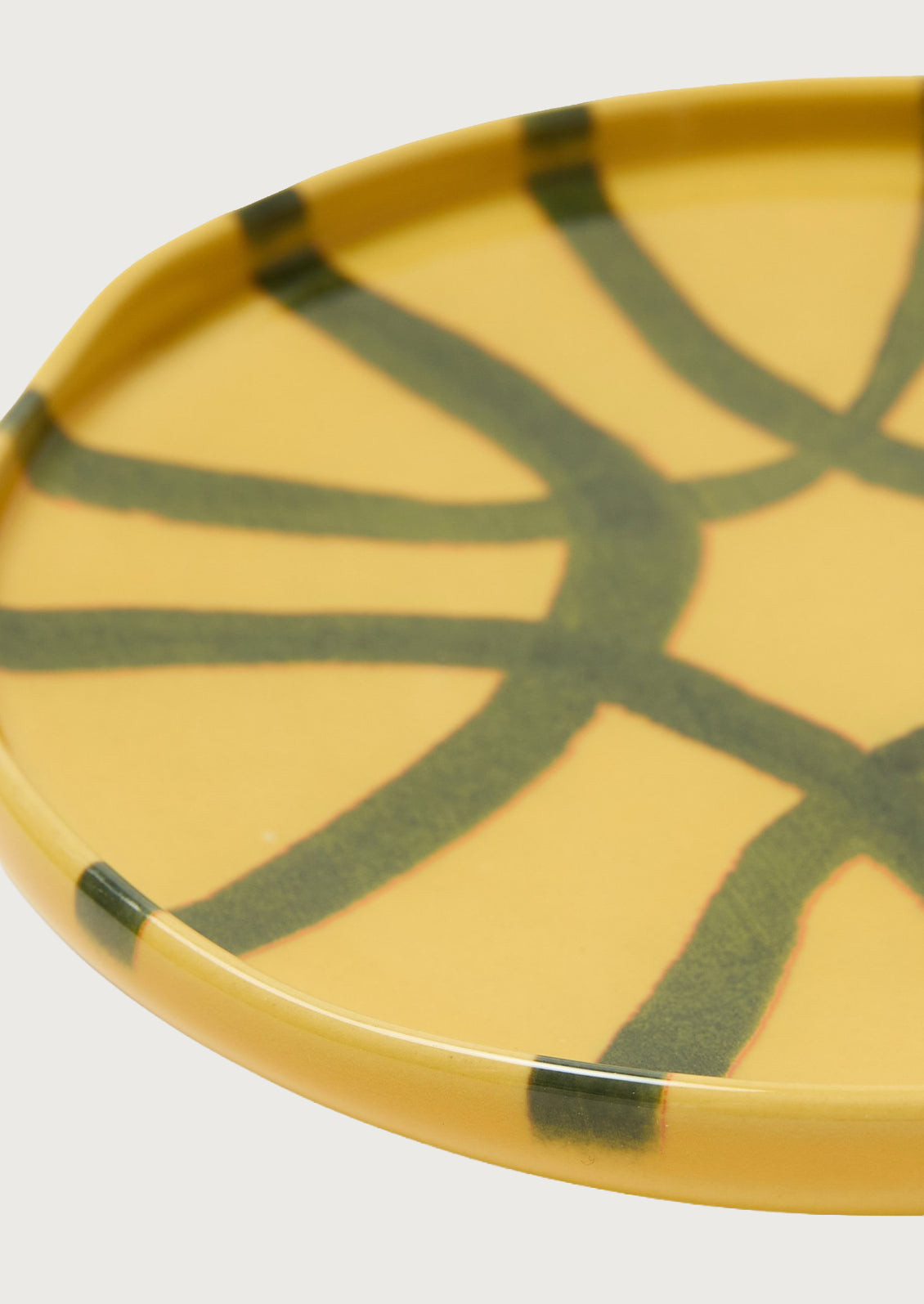 A ceramic side plate wth an abstract design in a marigold yellow color with dark green stripes.