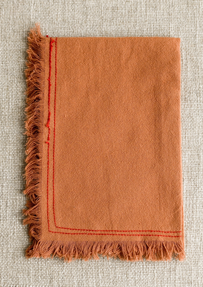 An orange tea towel with red stitching.