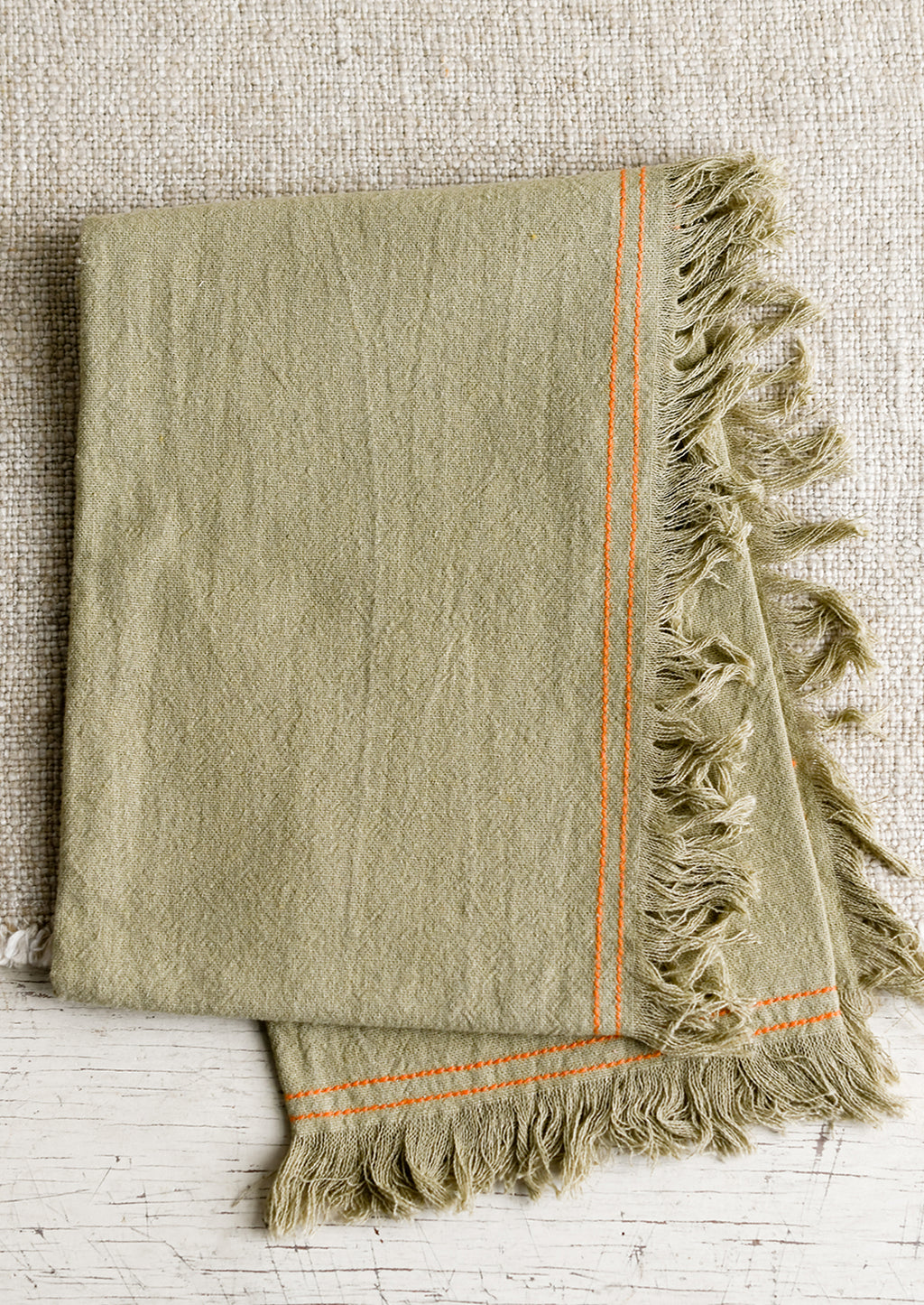 Sage: A green tea towel with orange stitching.