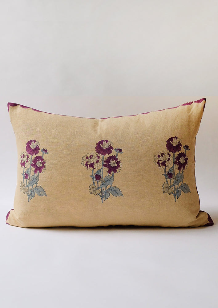 A lumbar throw pillow in sand color with purple flowers.