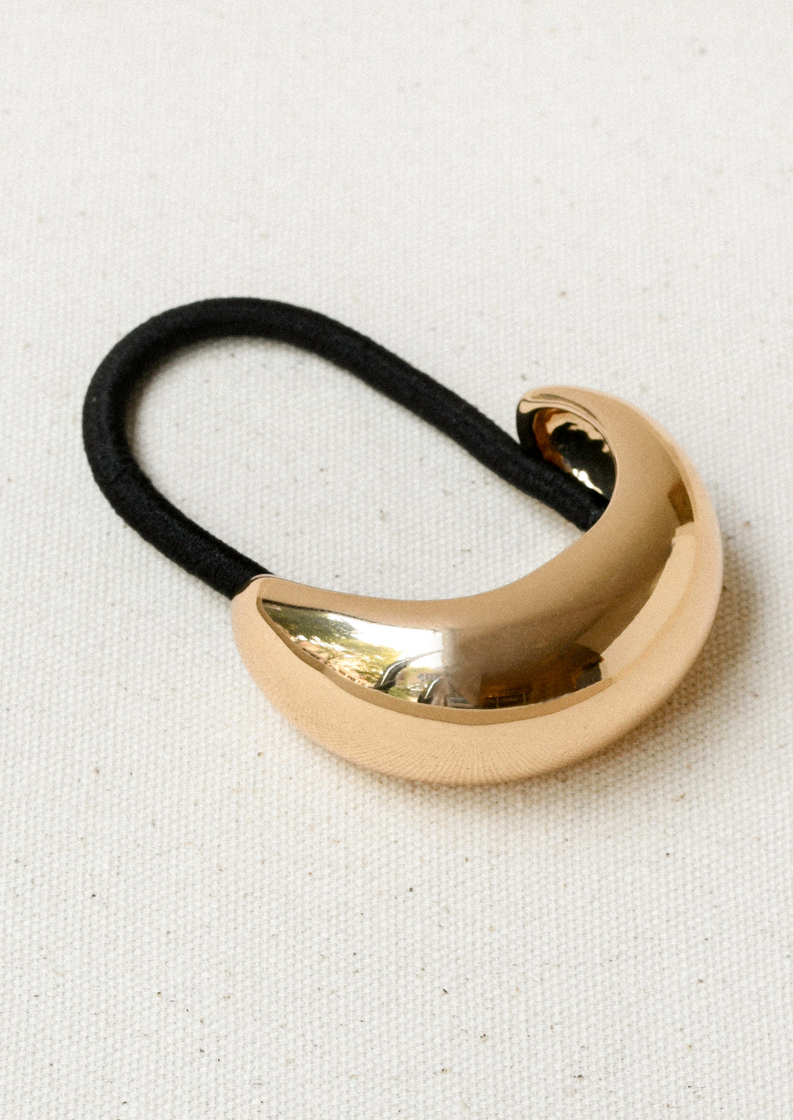A black elastic hair tie with a large gold crescent-shaped metal pendant.