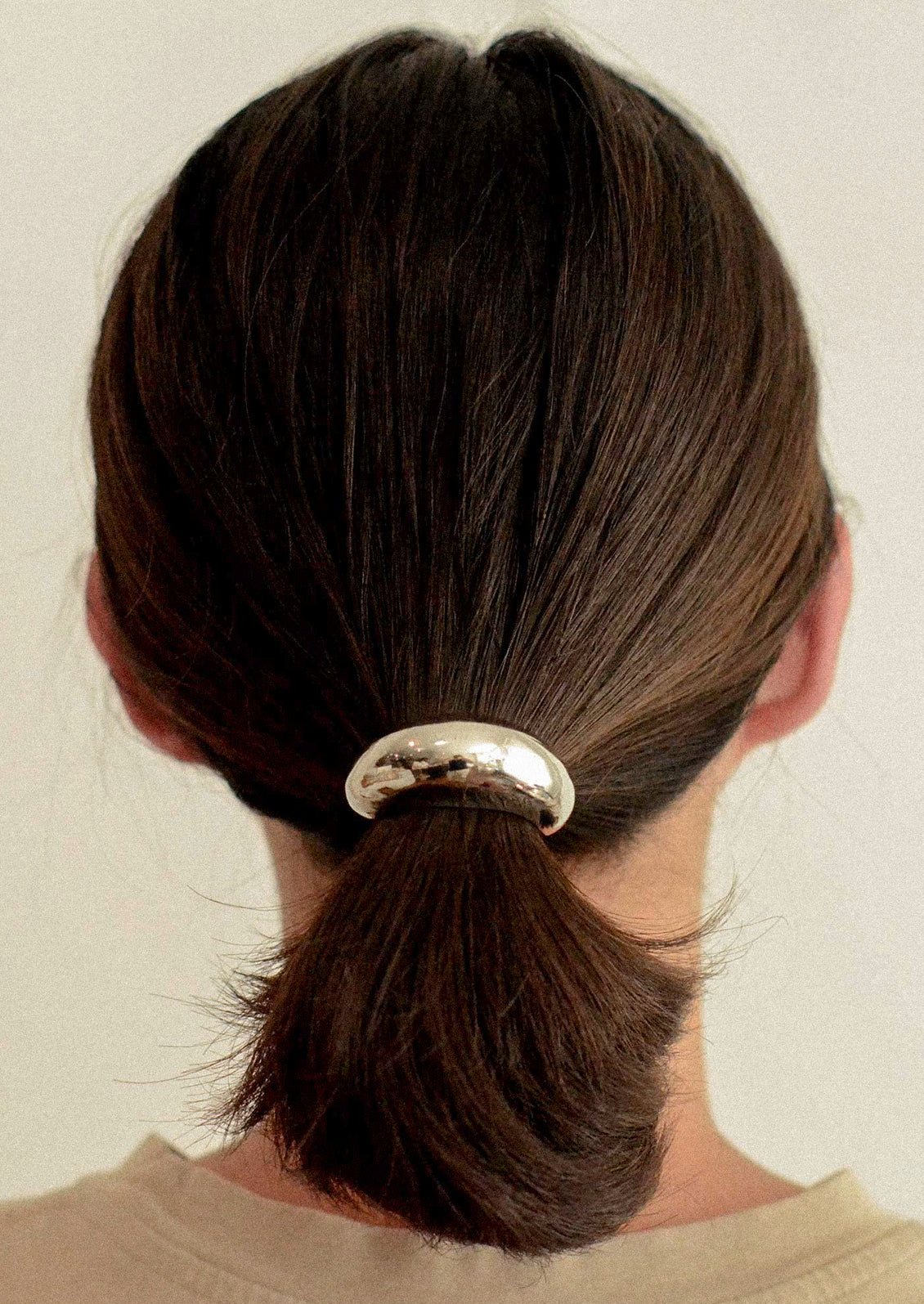A woman wearing an elastic hair tie with a large silver crescent-shaped metal pendant holding her ponytail.