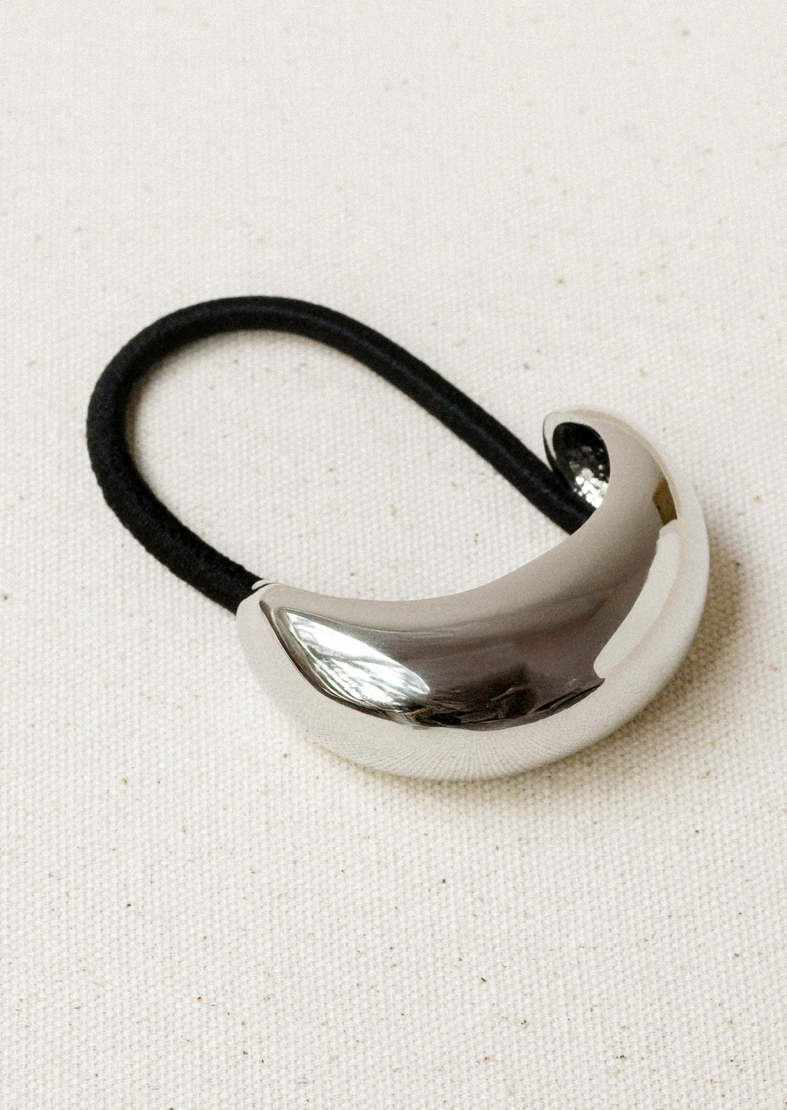 A black elastic hair tie with a large silver crescent-shaped metal pendant.