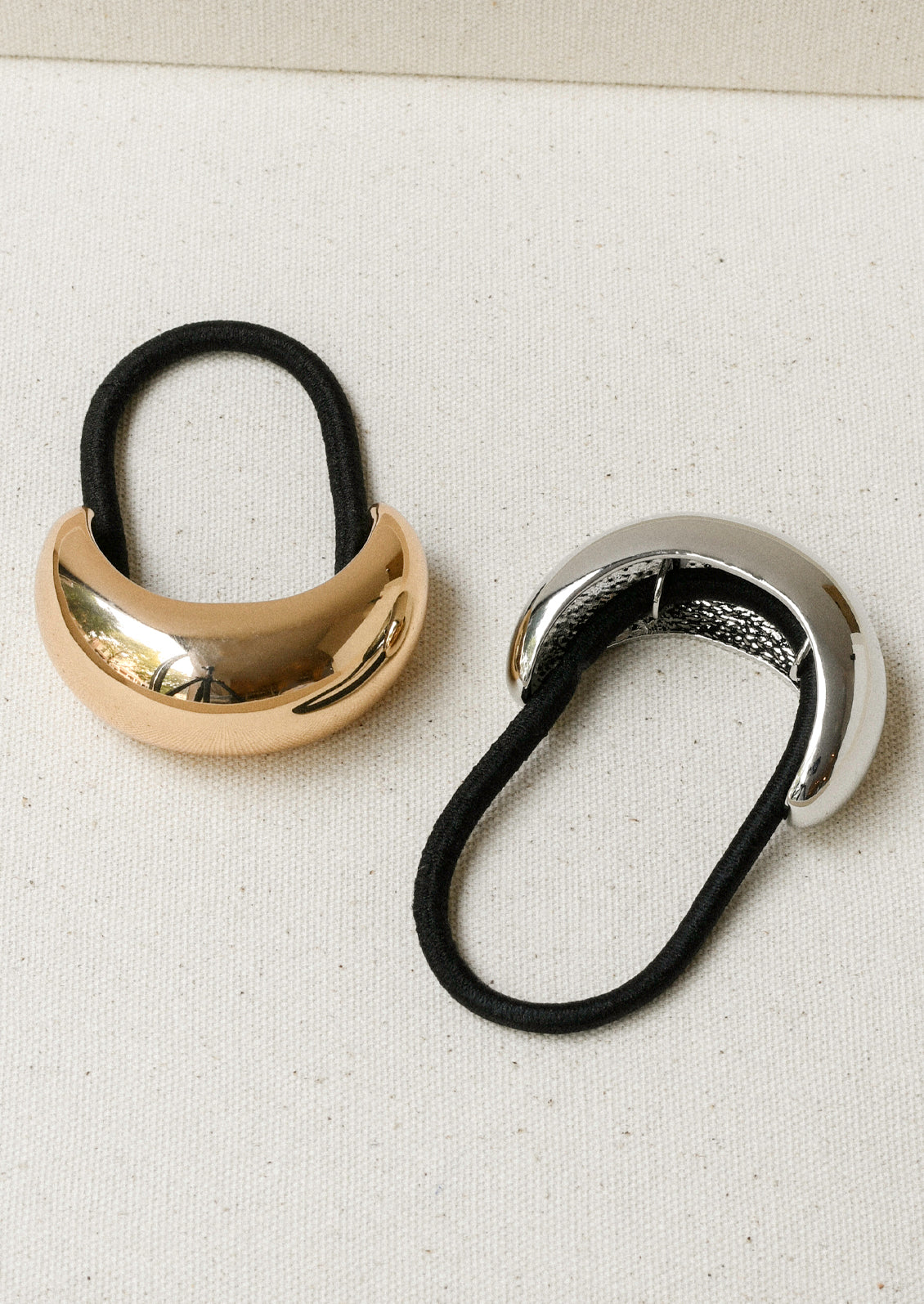 Two black elastic hair ties - one with a large gold crescent-shaped metal pendant and one in silver.