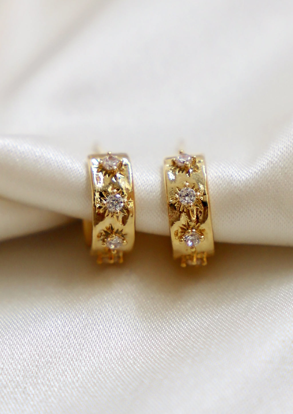 1: A pair of small gold hoop earrings with raised crystal starbust pattern.