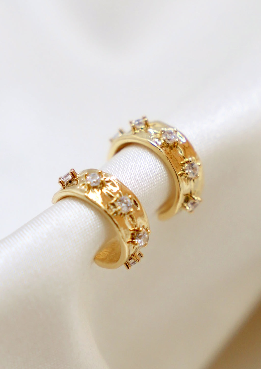 2: A pair of small gold hoop earrings with raised crystal starbust pattern.