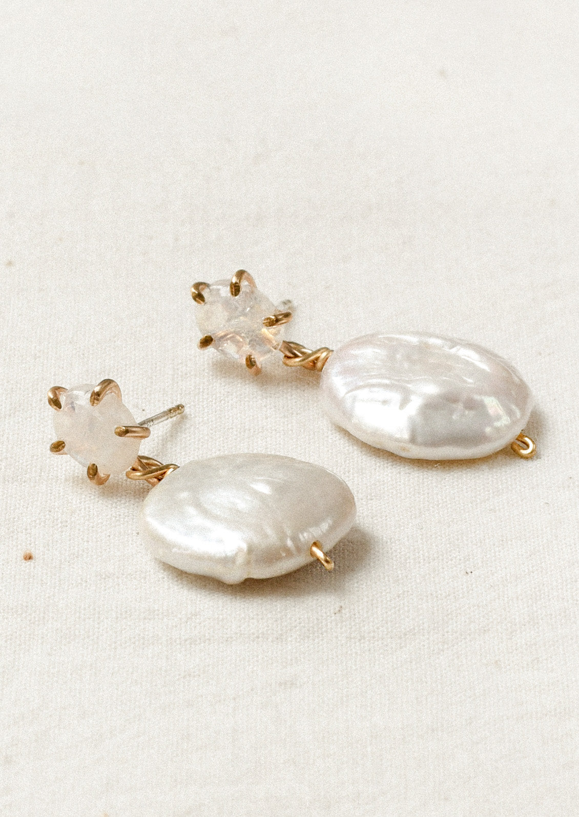 A pair of gold stud earrings feature a moonstone in a pronged setting with a large dangling freshwater coin pearl hanging below.