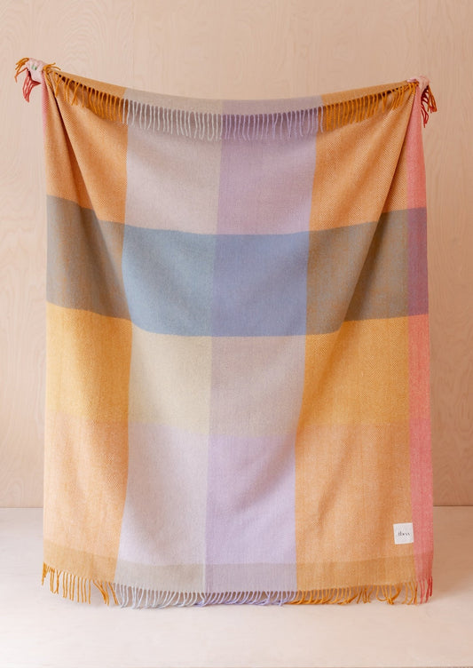 A colorful check patterned blanket in blue, orange, cream and pink tones.