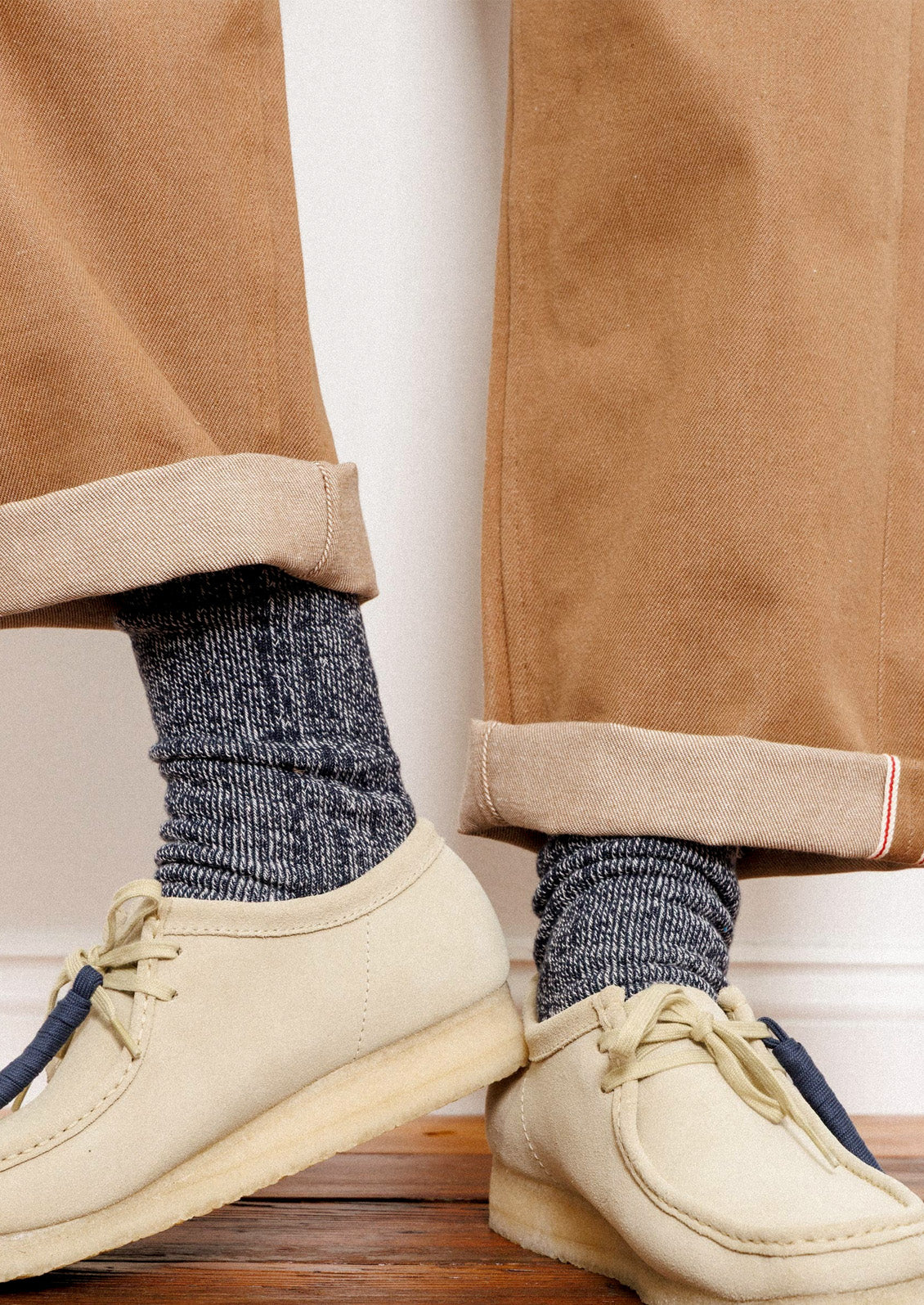 A person wearing brown pants, ivory boat shoes, and marled navy socks.
