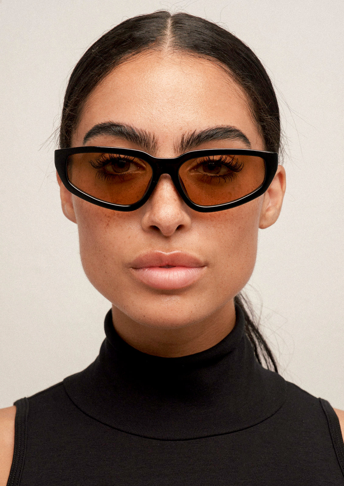 A woman wearing a pair of angular cat eye sunglasses with a black frame and light brown lenses.