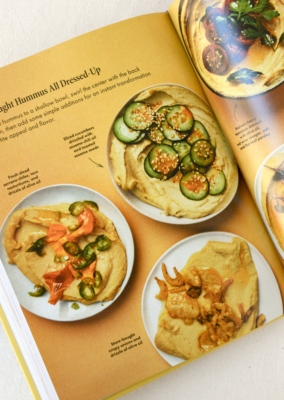 A cookbook open on a table with images of hummus with various dressings.