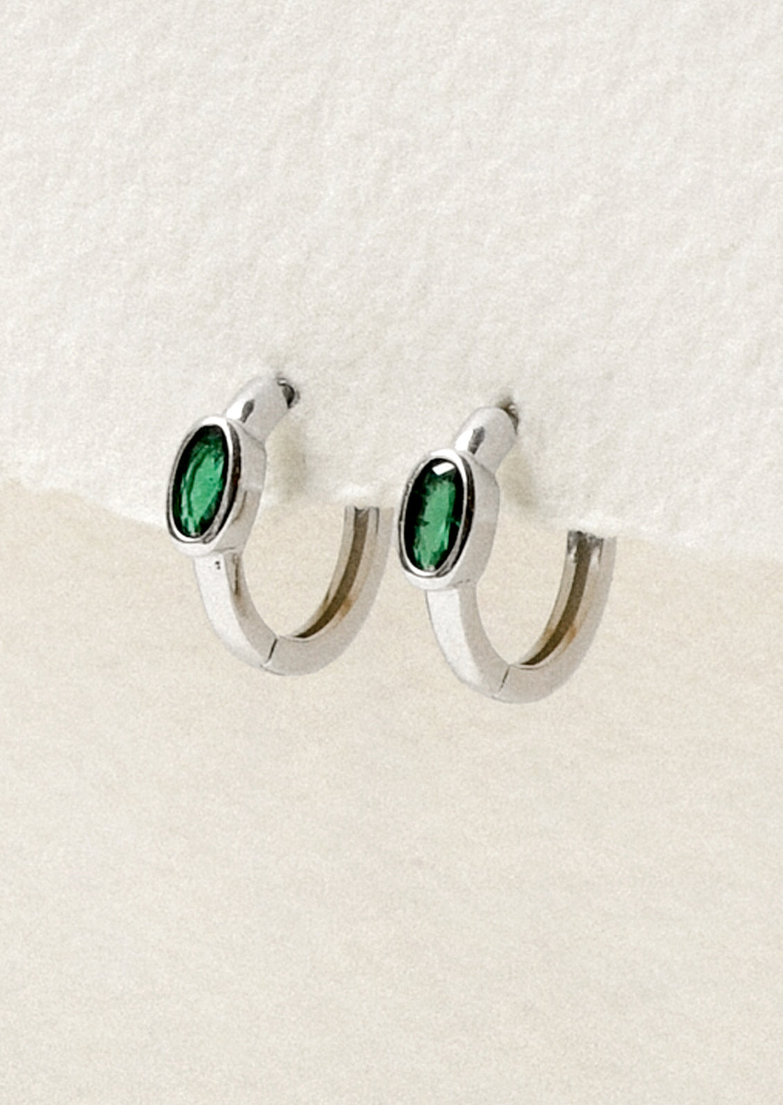 A pair of sterling silver hoop earrings with a green oval gemstone.