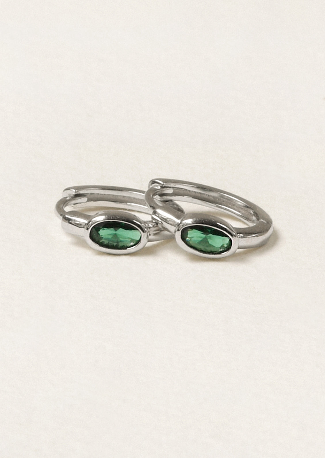 A pair of sterling silver hoop earrings with a green oval gemstone.