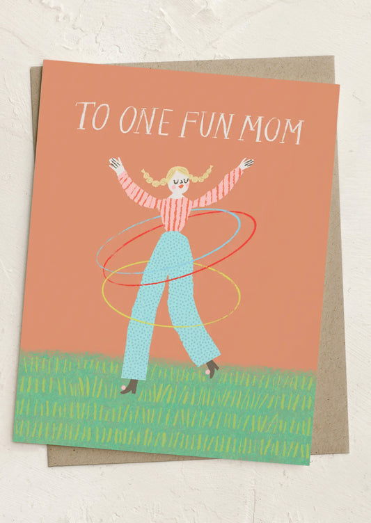 Greeting card with illustration of a woman hula hooping and text 'To One Fun Mom' on a peach background.