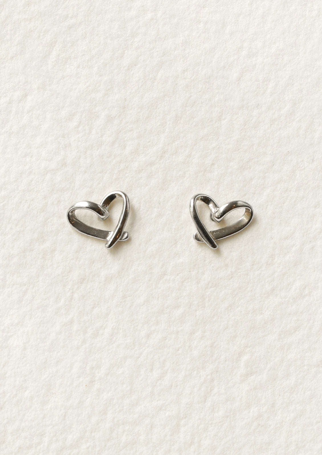 A pair of sterling silver stud earrings that are bent in the shape of hearts.