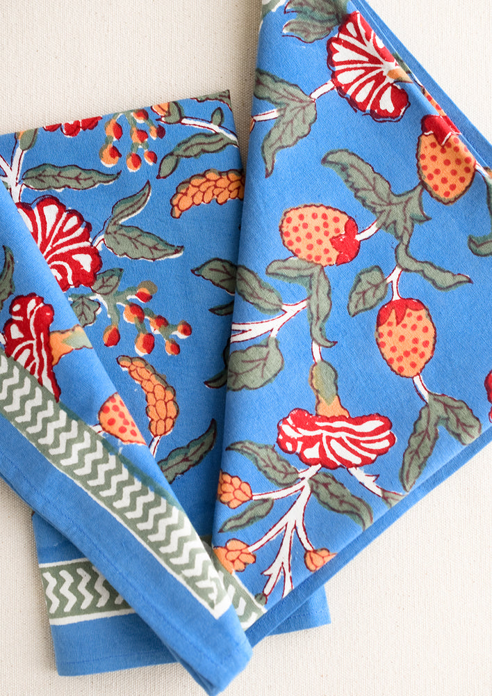 A pair of blue napkins with block printed fruit/flower pattern in orange and red.