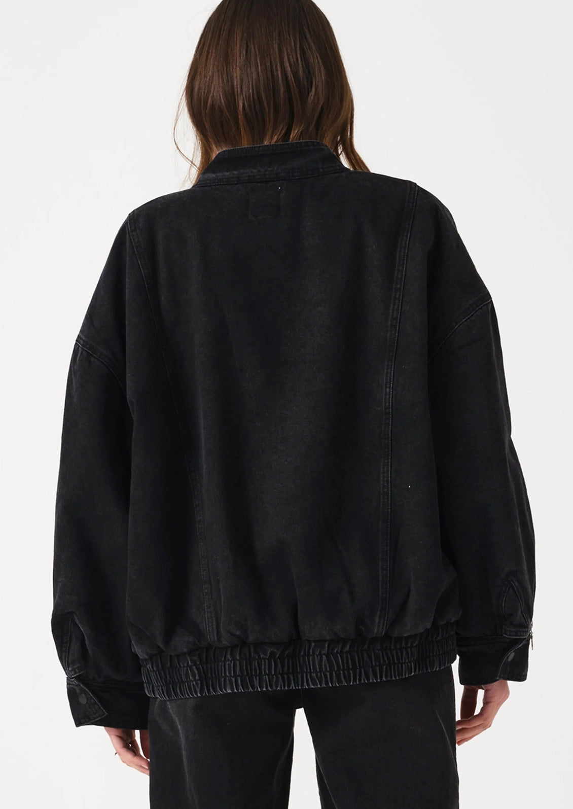 A person shown from the back wearing an oversized black jacket with a gathered elastic hem and cuffs, paired with black pants, against a plain light background.