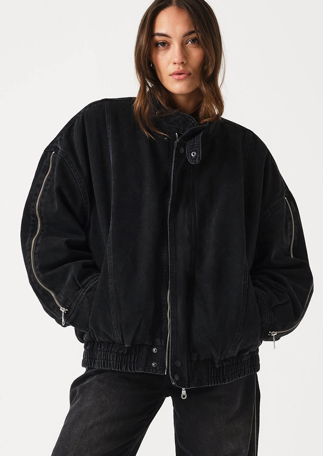 A model wearing a black oversized zip-up jacket with light-colored contrast stitching and black jeans, photographed against a clean white studio background.
