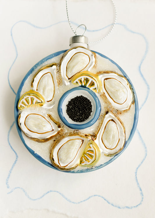 A round glass ornament depicting a tray of oysters, lemons and black caviar.