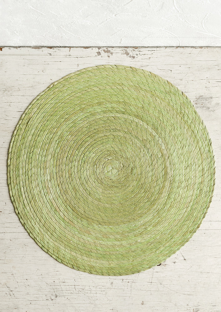 A round woven straw placemat in pistachio color.