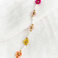 3: A white beaded bracelet with pink and yellow beaded flowers.