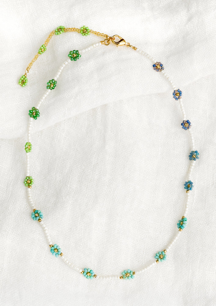 1: A beaded necklace with white beads and blue and green beaded flowers.