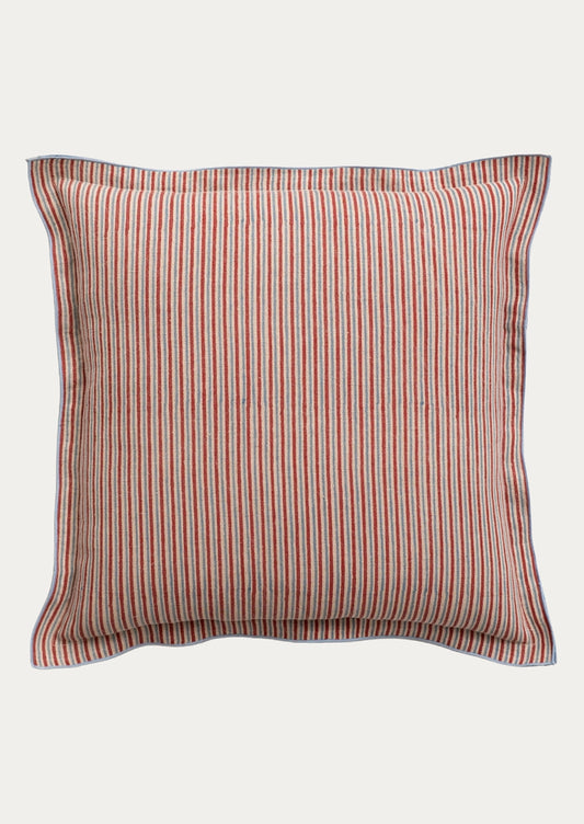 A square throw pillow with vertical red and blue stripes on a beige fabric background, finished with a solid blue piped border.