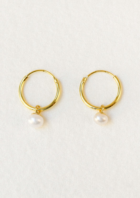 A pair of gold hoop earrings with a dangling freshwater pearl charm.