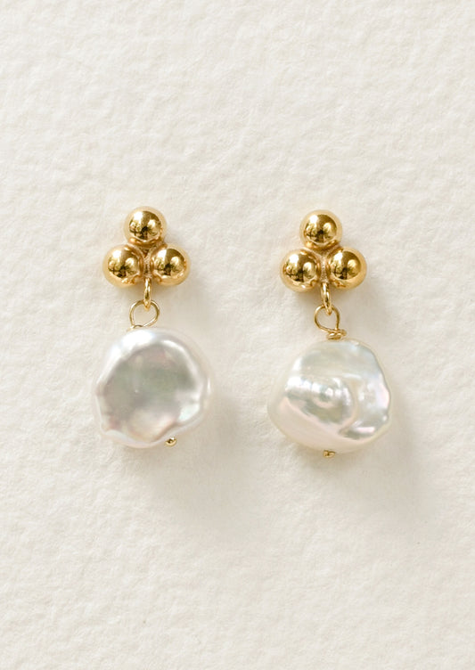 A pair of stud earrings featuring three round dots at the top and a dangling freshwater pearl.