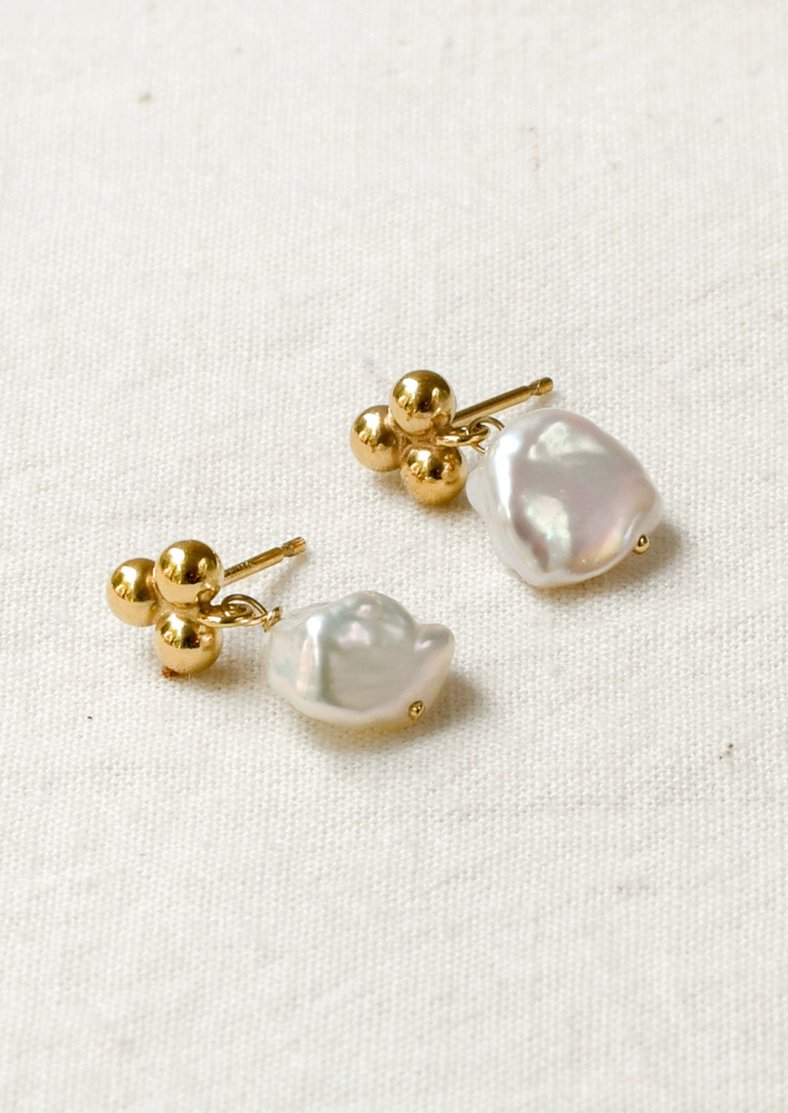 A pair of stud earrings featuring three round dots at the top and a dangling freshwater pearl.