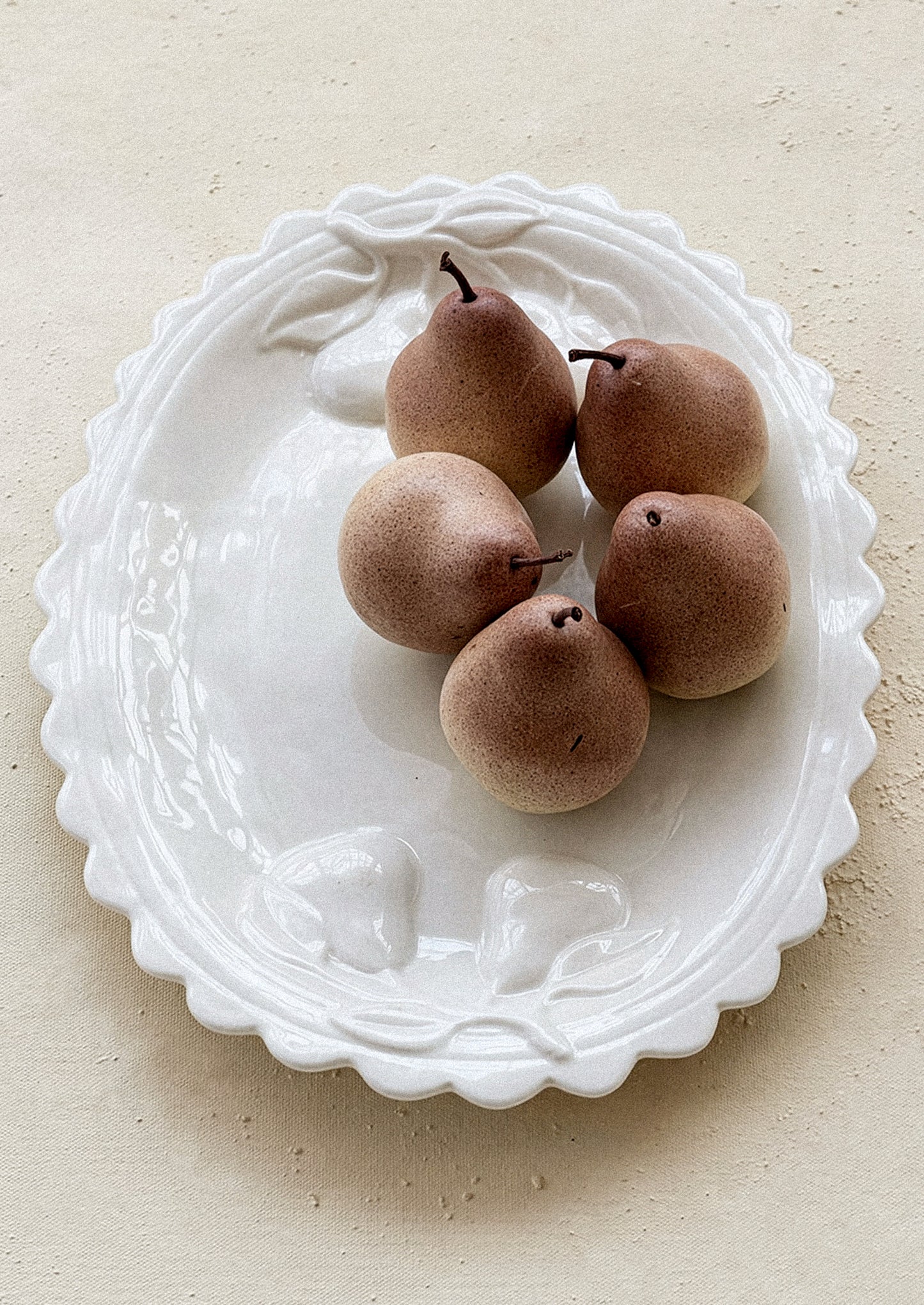 Five brown pears on a decorative white plate with scalloped edges.