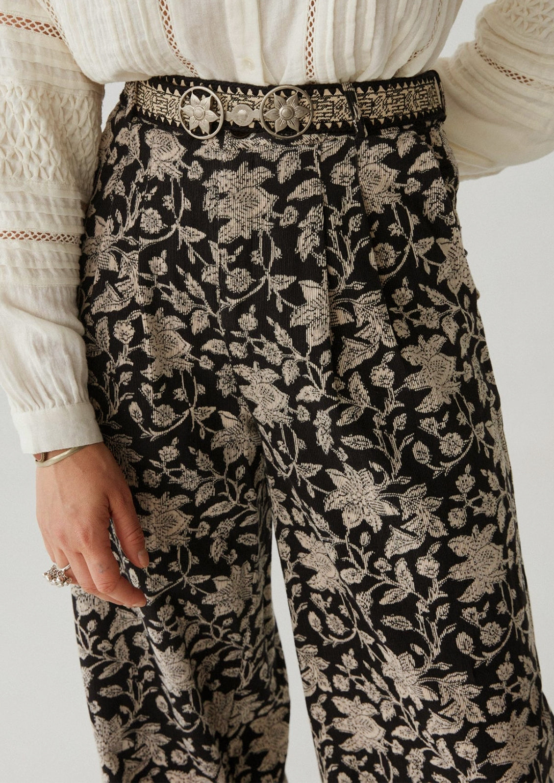 A woman wearing a pair of paisley floral print corduroy pants in black with white flowers.