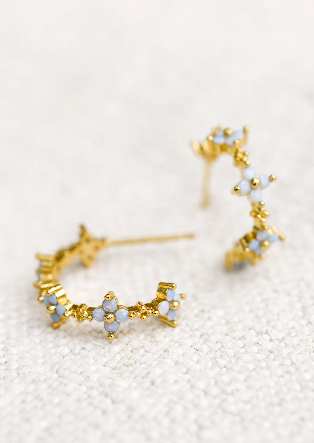 2: A pair of gold hoop earrings with periwinkle opal blue flowers.