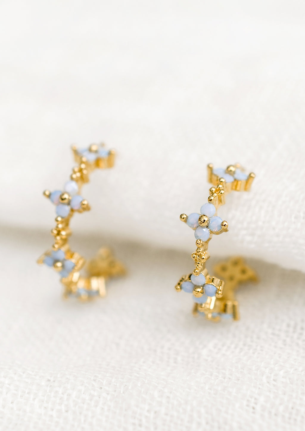 1: A pair of gold hoop earrings with periwinkle opal blue flowers.