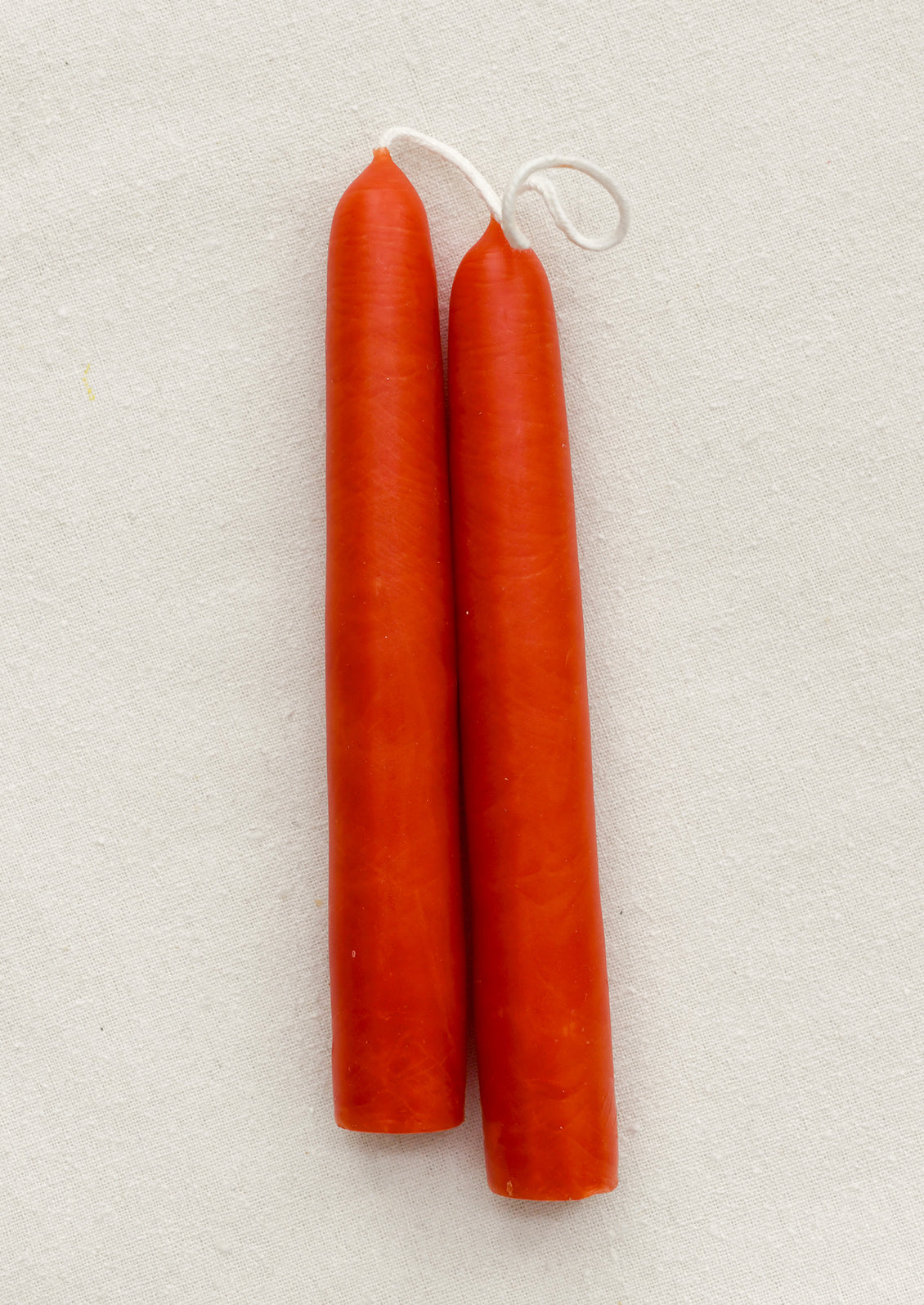 A pair of short red-orange taper candles on a brown background.