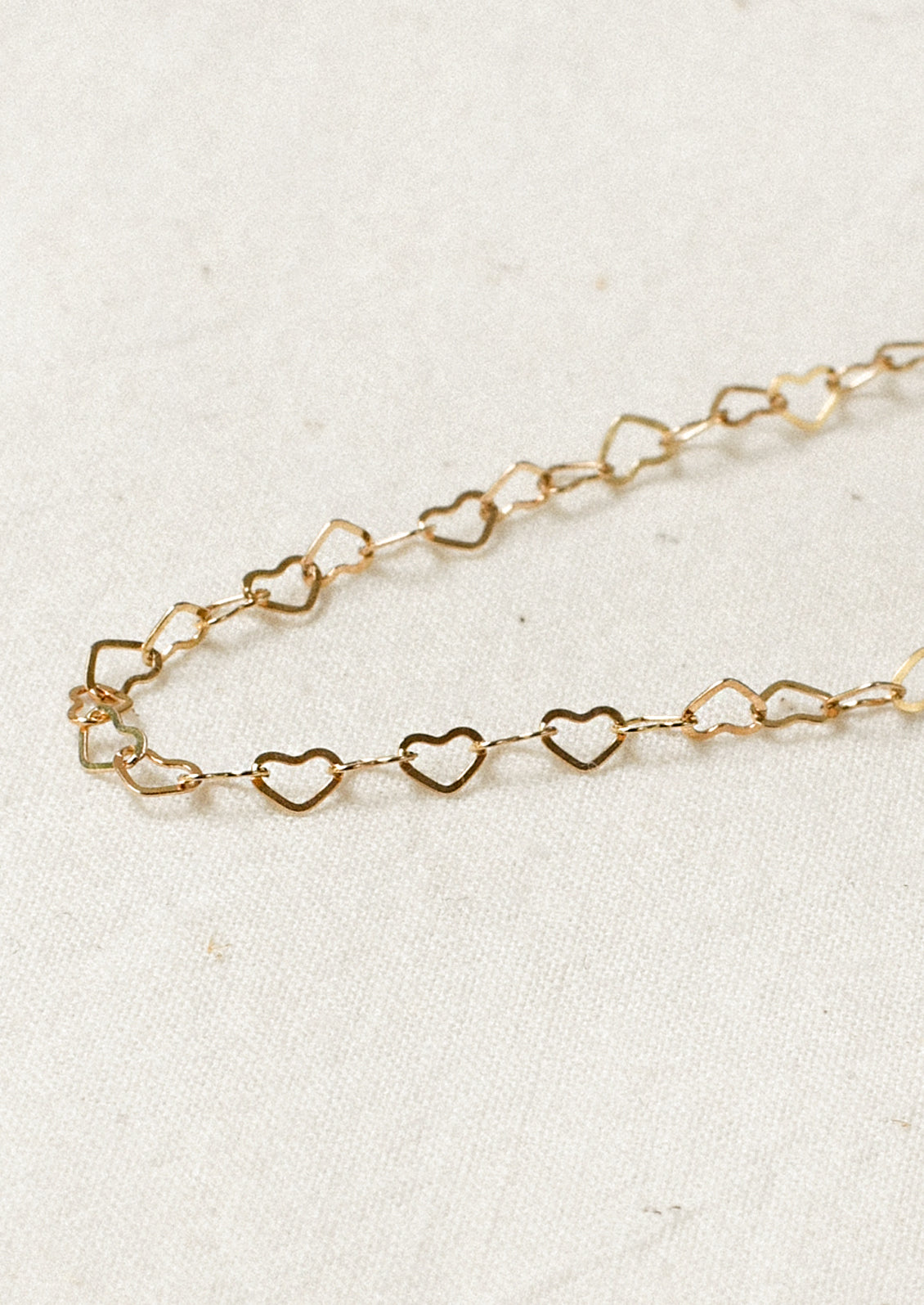 A gold necklace composed of tiny hearts linked together in a chain.