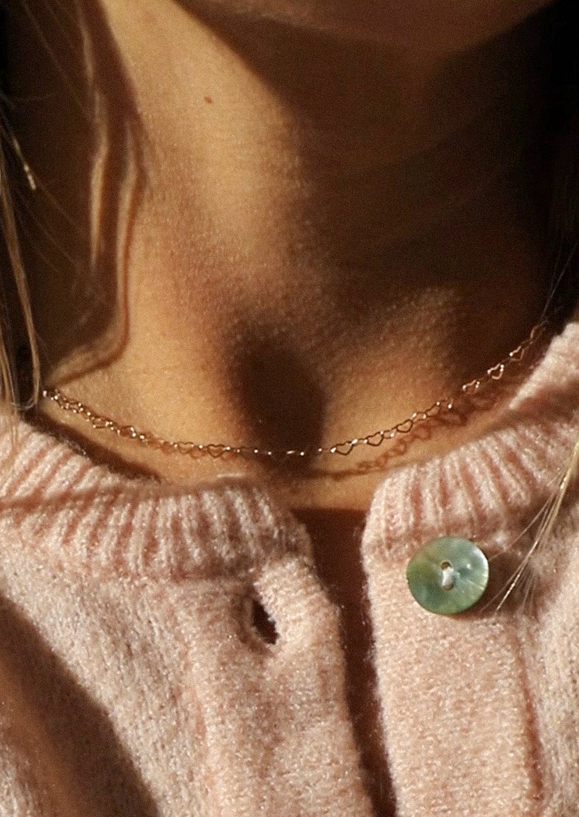 A woman wearing a pink garden and a gold heart chain necklace.