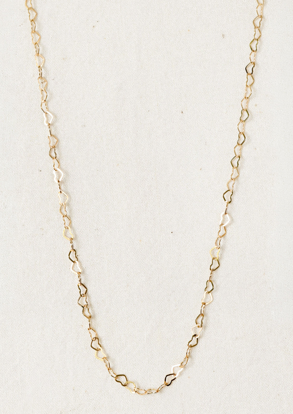 A gold necklace composed of tiny hearts linked together in a chain.