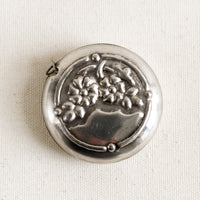 Pewter Flowers: A round silver-tone measuring tape with embossed floral pattern.