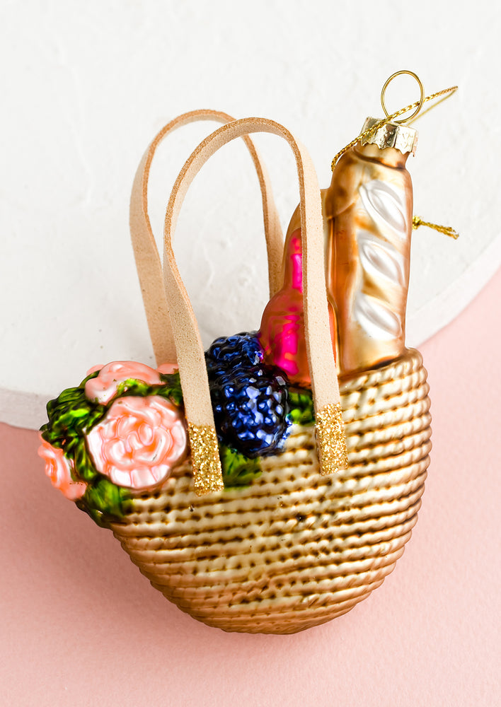 1: A glass ornament of a straw tote with picnic supplies.