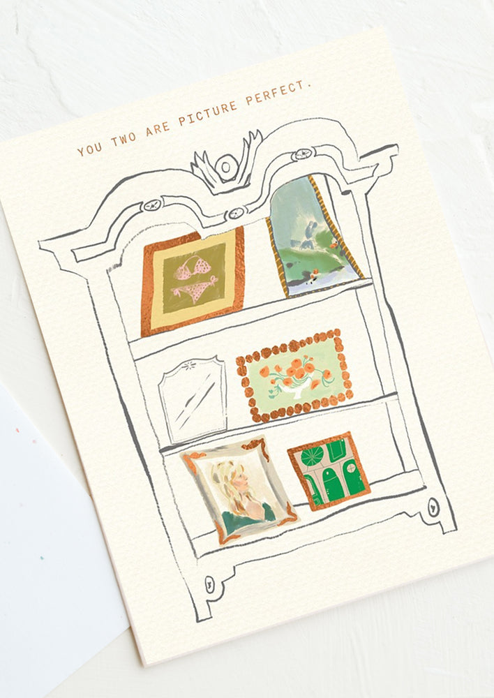 A card with illustration of art on a bookshelf, text reads "You two are picture perfect".