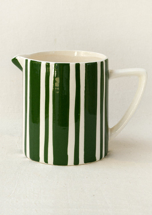 A ceramic pitcher with a handle and spout, decorated with vertical dark green and white stripes, set against a plain off-white background.