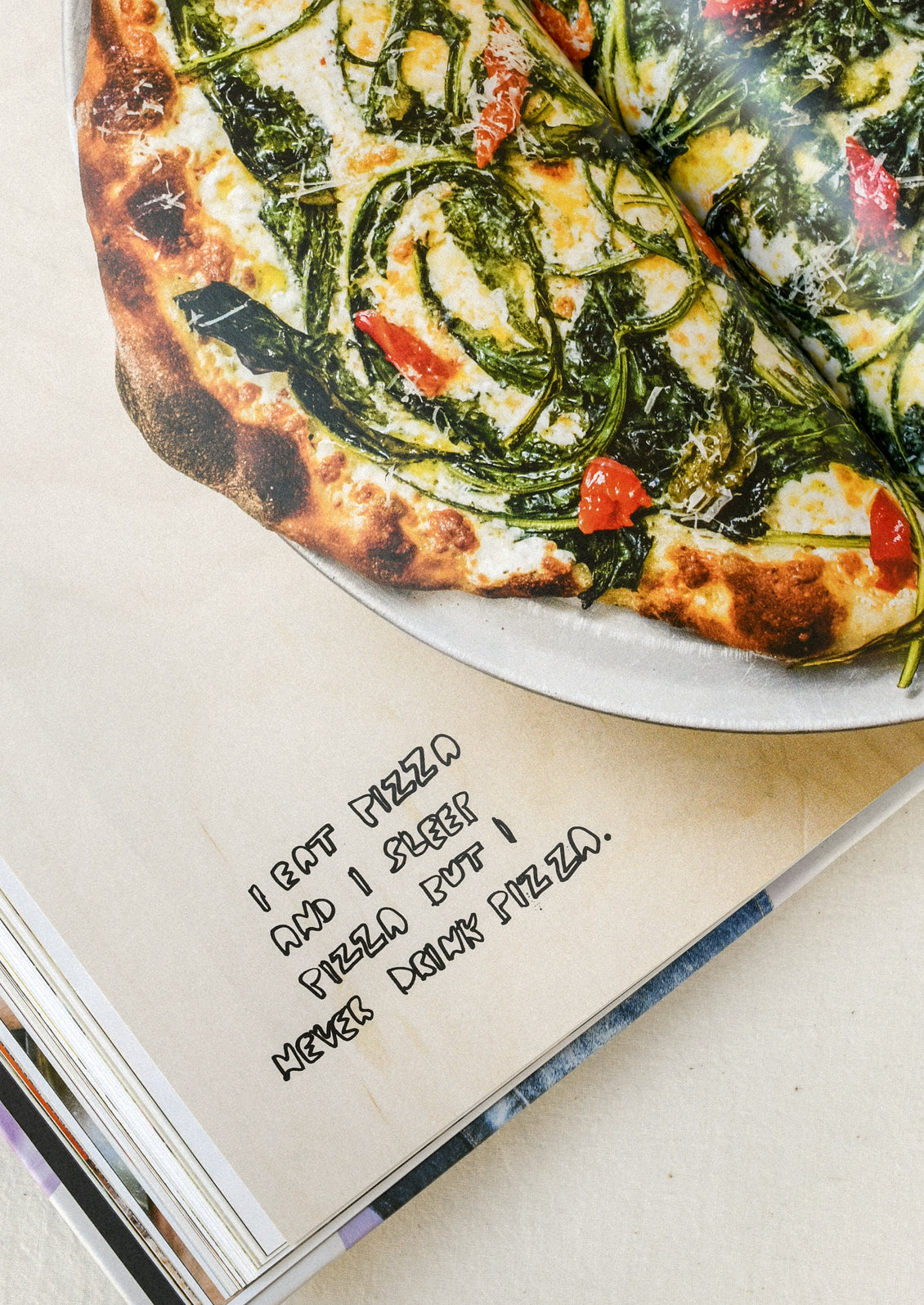 A book open on a table with an image of a pizza and the words "I eat pizza and I sleep pizza but I never drink pizza."