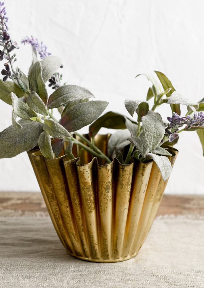 A pleated metal planter in distressed brass finish.