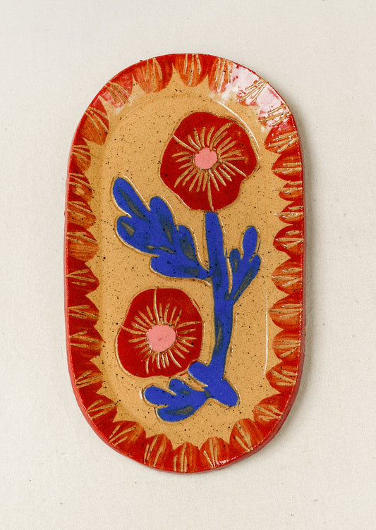 A ceramic oval catchall tray with an etched red poppy flower in the center and a red painted border.